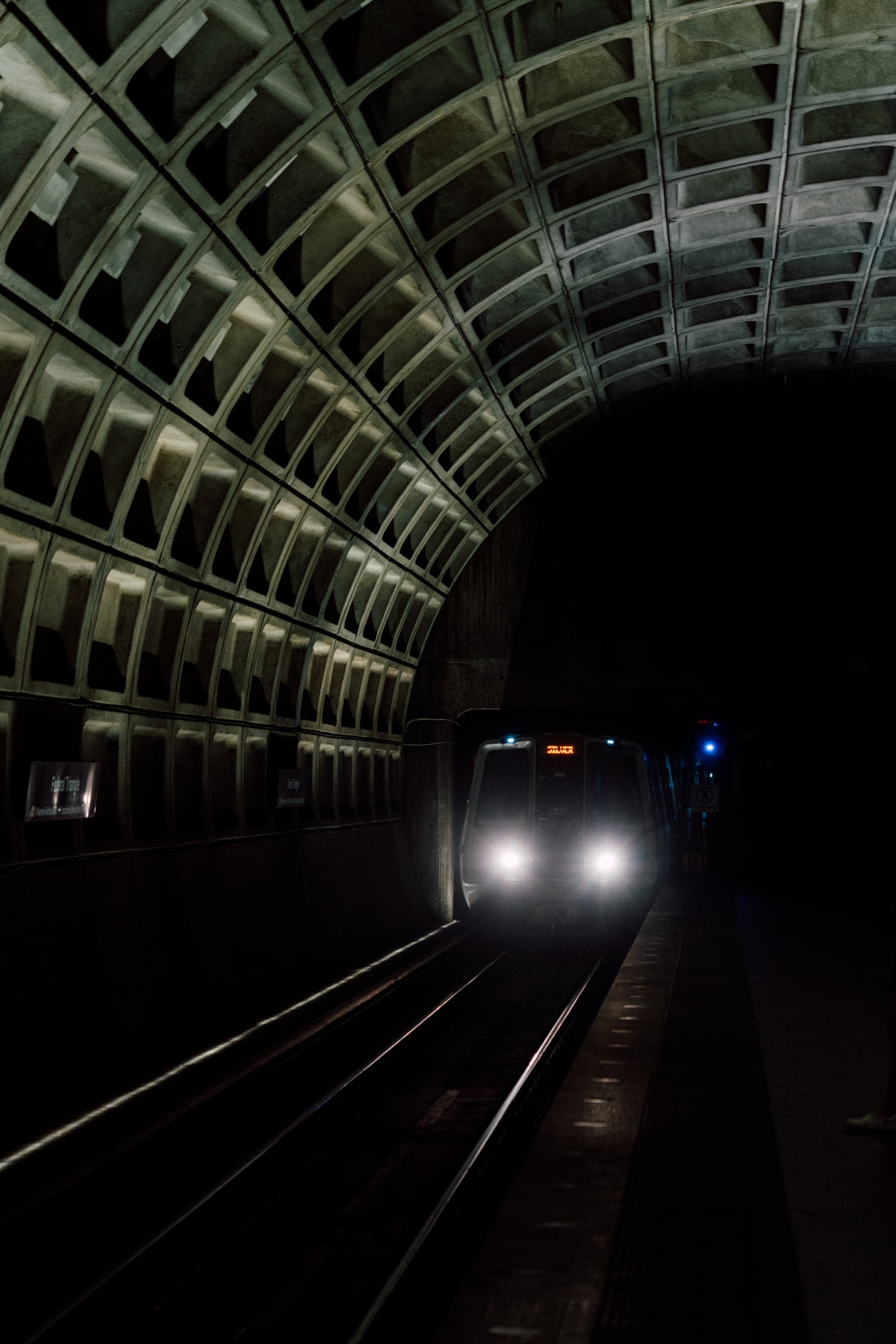 A subway train approaches in a dimly lit underground station with a vaulted ceiling