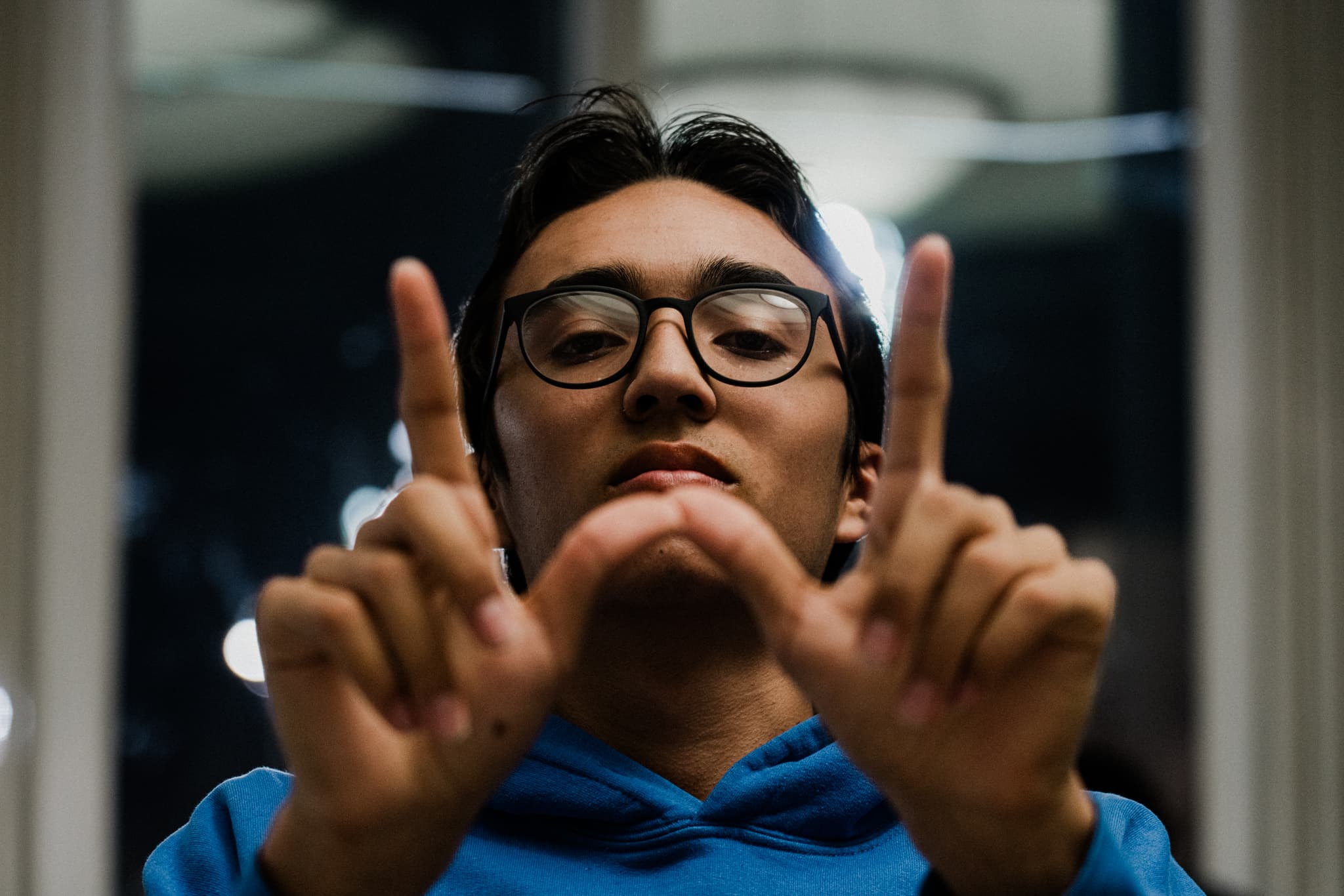 A person in a blue hoodie is making a hand gesture that resembles a frame, possibly mimicking the act of composing a photograph or focusing on something through an imaginary viewfinder