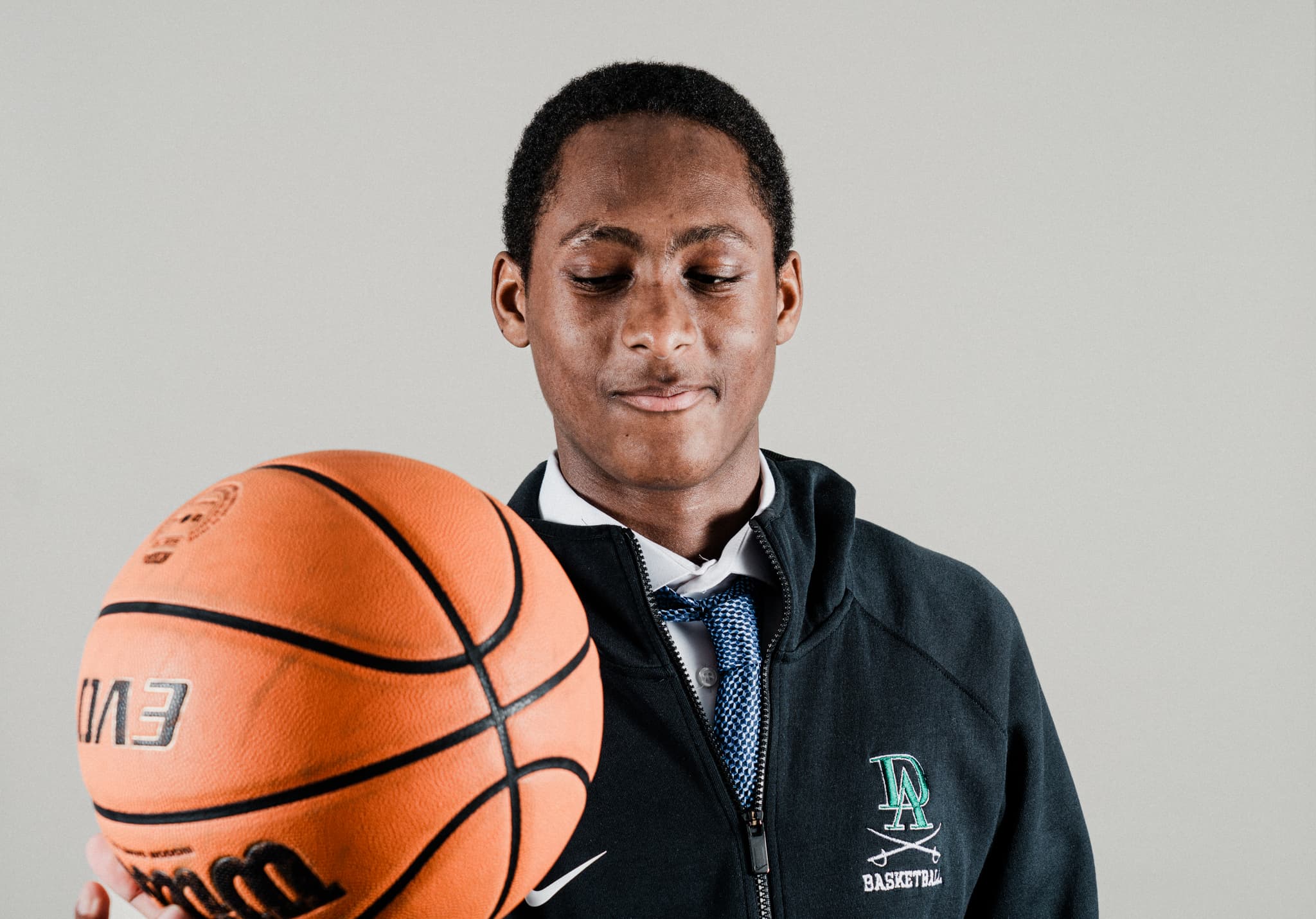 A person in a sports jacket is spinning a basketball on their finger, looking at it with a focused expression