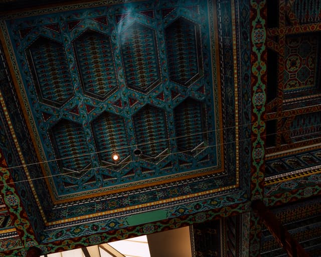 An ornately decorated ceiling with intricate geometric patterns and vibrant colors, likely from an architectural structure with traditional or historical significance