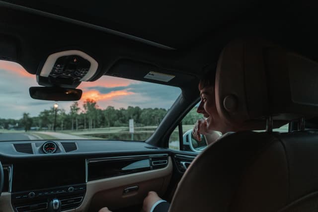 A person driving a car during sunset, with the interior of the vehicle and the rearview mirror visible