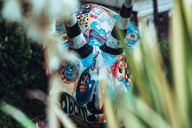 A colorfully painted elephant sculpture partially obscured by foliage in the foreground