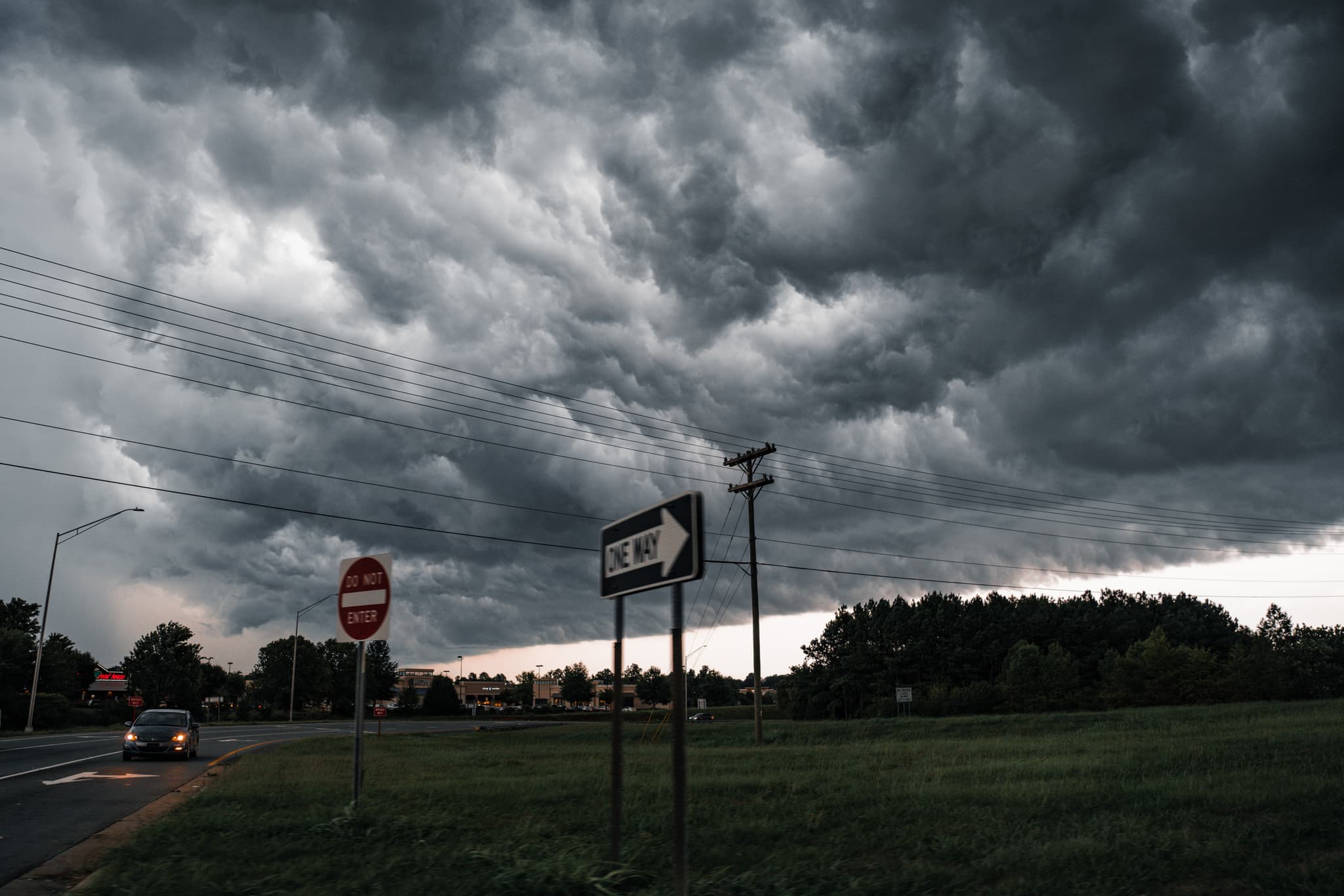 Dark storm clouds loom over a road with a stop sign and streetlights, suggesting an impending storm