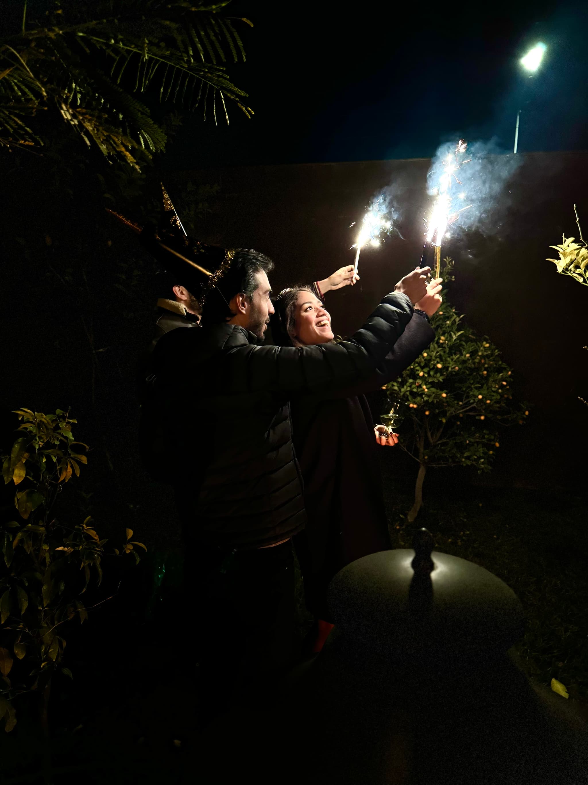 Three people holding sparklers, celebrating outdoors at night