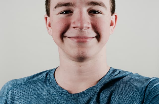 A smiling young person wearing a blue t-shirt against a light background