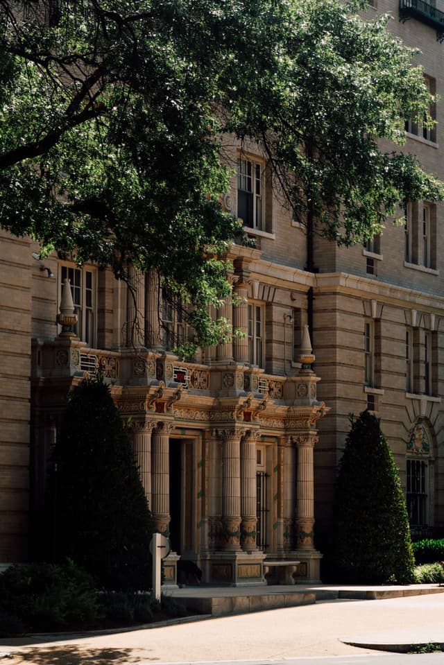 A classic architectural facade with ornate detailing, flanked by trees under bright sunlight