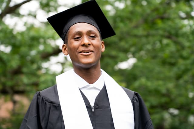 A smiling graduate wearing a cap and gown outdoors