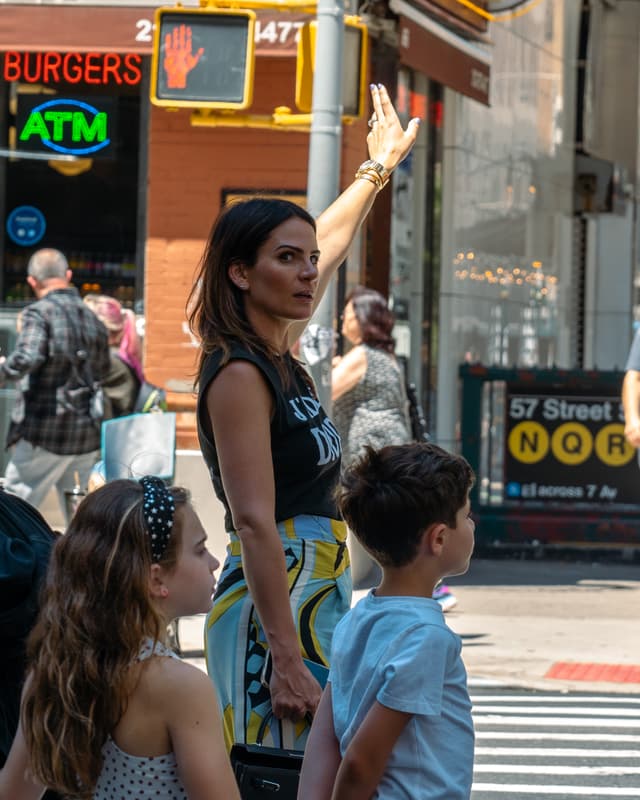 A woman is raising her arm to hail a taxi on a busy city street while accompanied by two children