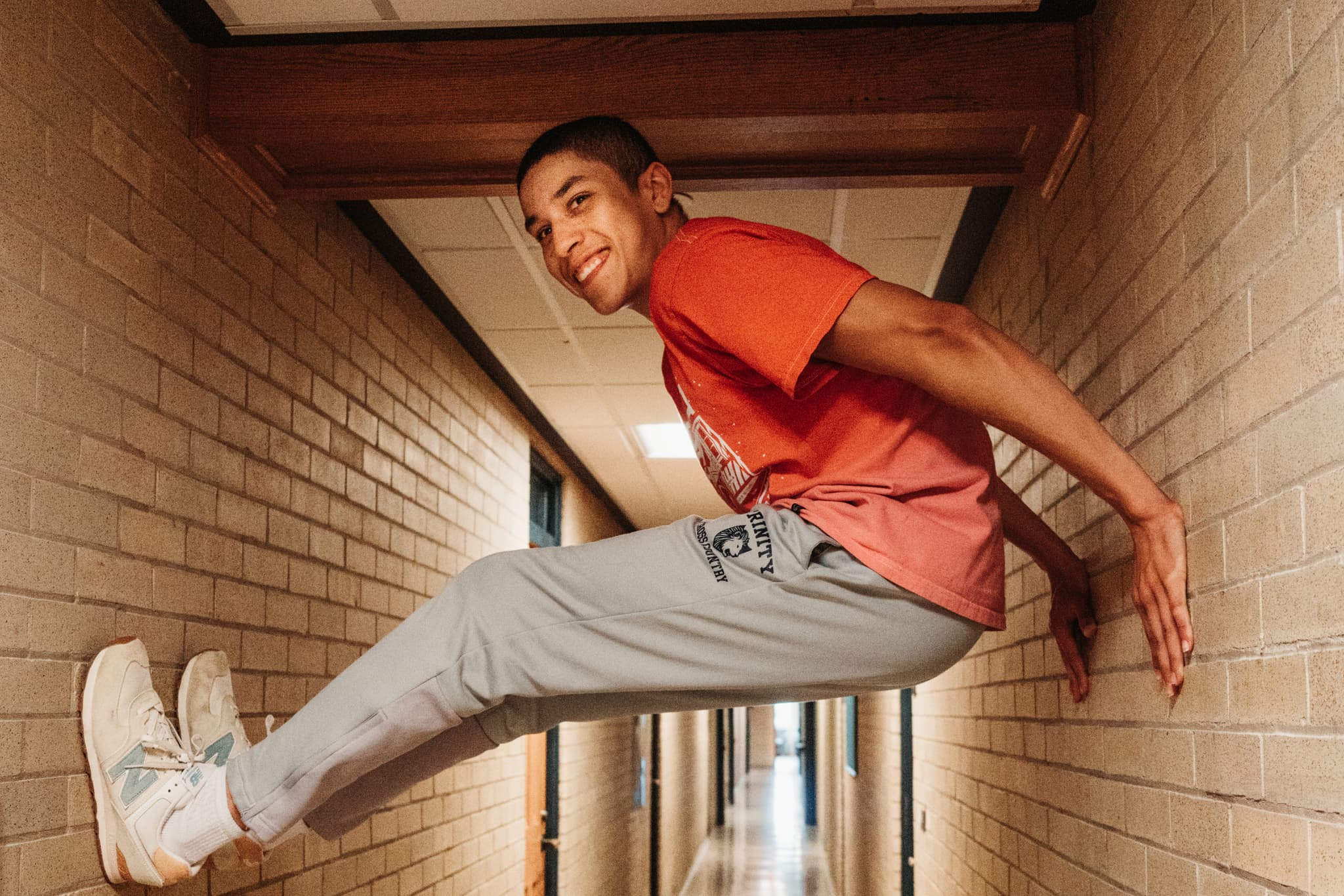 A person is bracing themselves between two walls in a narrow corridor, appearing to defy gravity with a relaxed posture and a smile