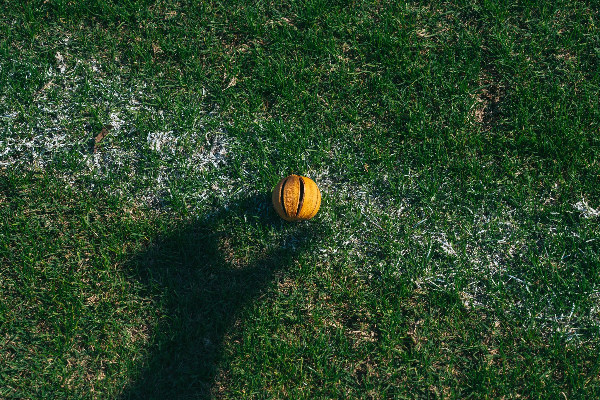 A basketball lies on a grassy surface, casting a shadow