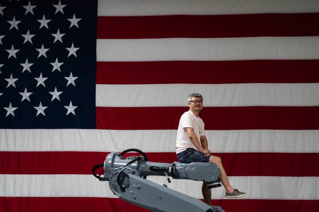 A person sits on a piece of gym equipment in front of a large American flag