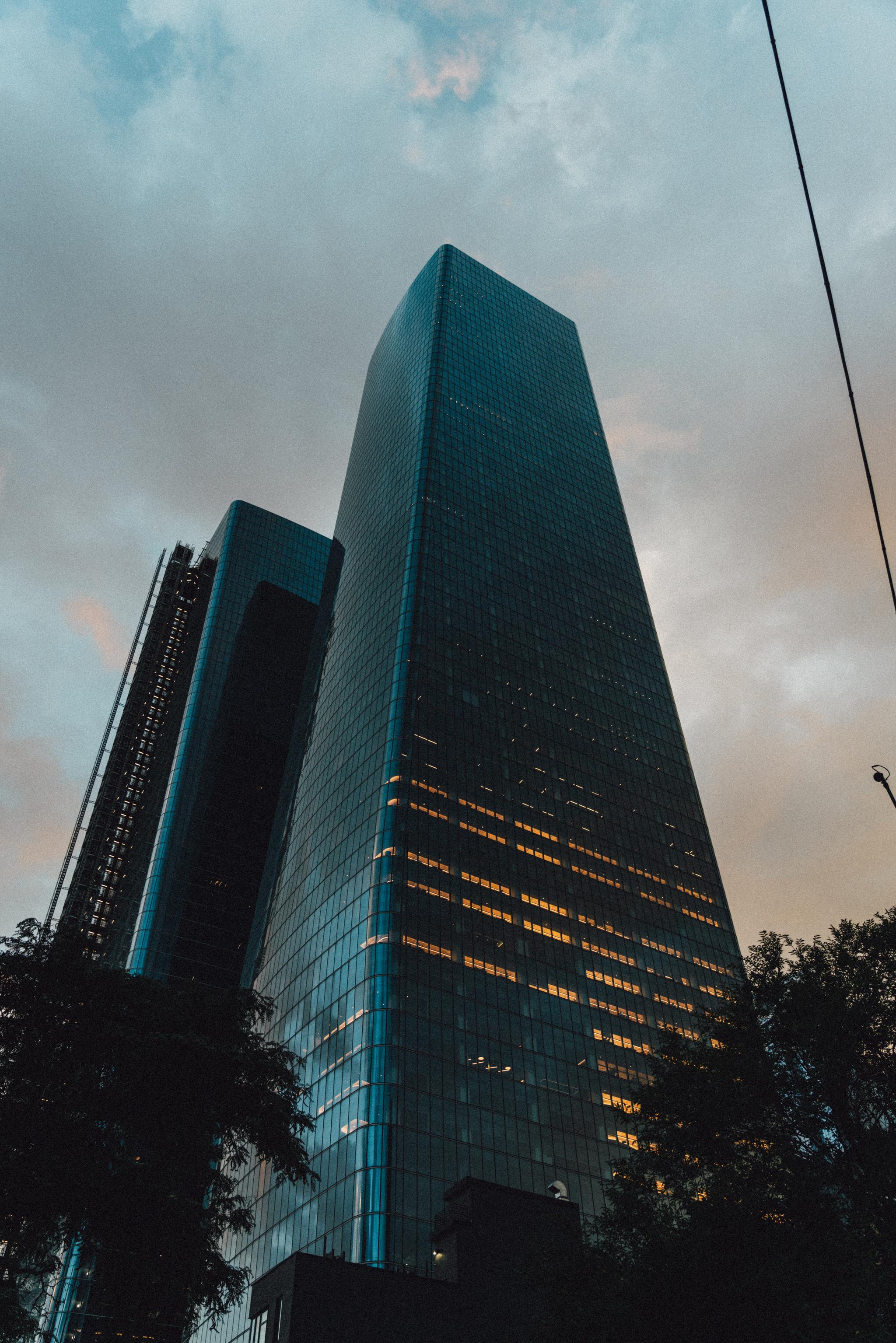 A towering skyscraper dominates the frame against a dusky sky, with lights visible in some of its windows