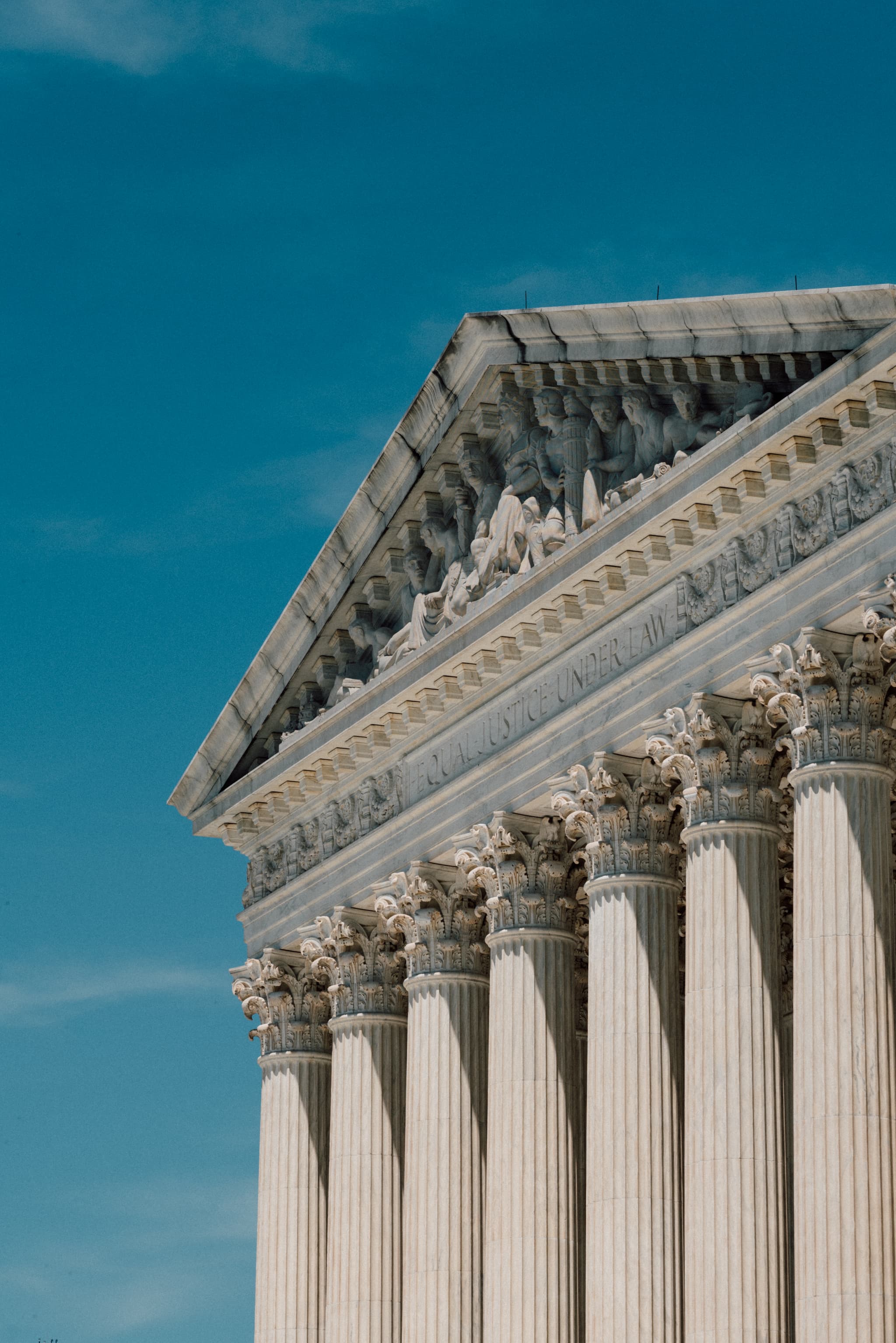 A neoclassical building's facade with Corinthian columns and a detailed pediment against a clear blue sky