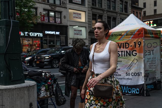 A woman walks on a city street with a COVID-19 testing sign in the background