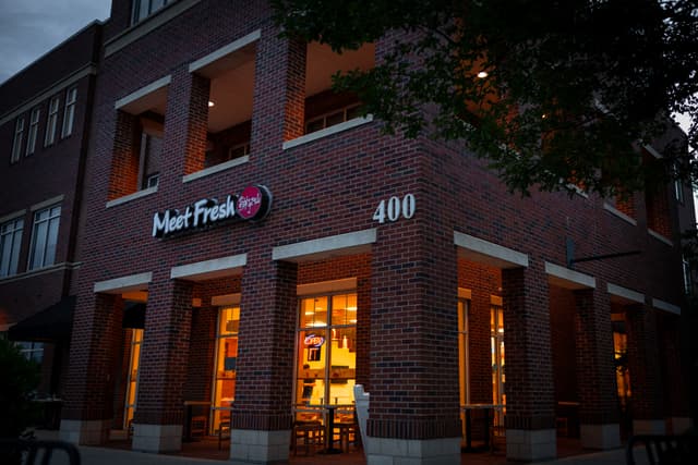 A two-story brick building at dusk with warm interior lighting visible through the windows, a sign with the name Harr Fresh on the upper left, and the street number 400 displayed prominently