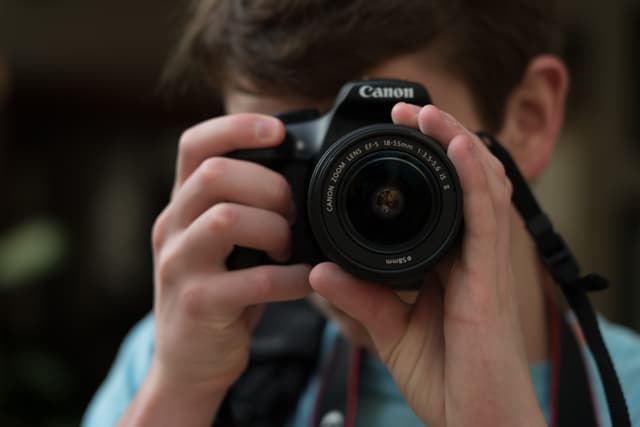 A person holding a Canon camera up to their face, presumably taking a photograph