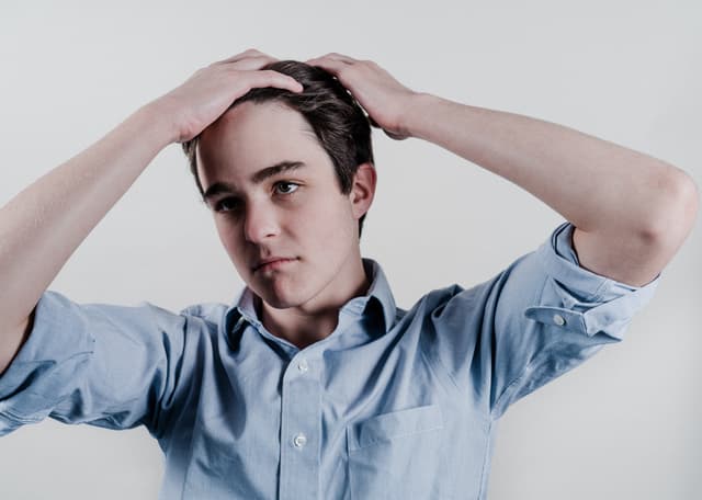 A young man in a blue shirt with his hands on his head, possibly in a gesture of concern, confusion, or exasperation