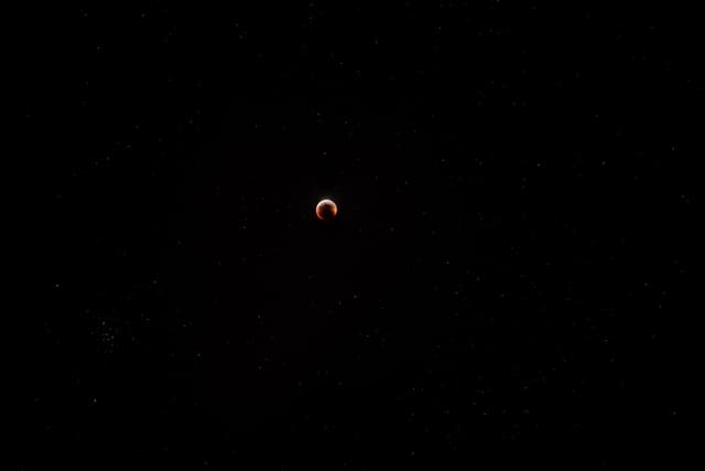 A lunar eclipse captured against a dark sky, with the moon appearing in a reddish hue