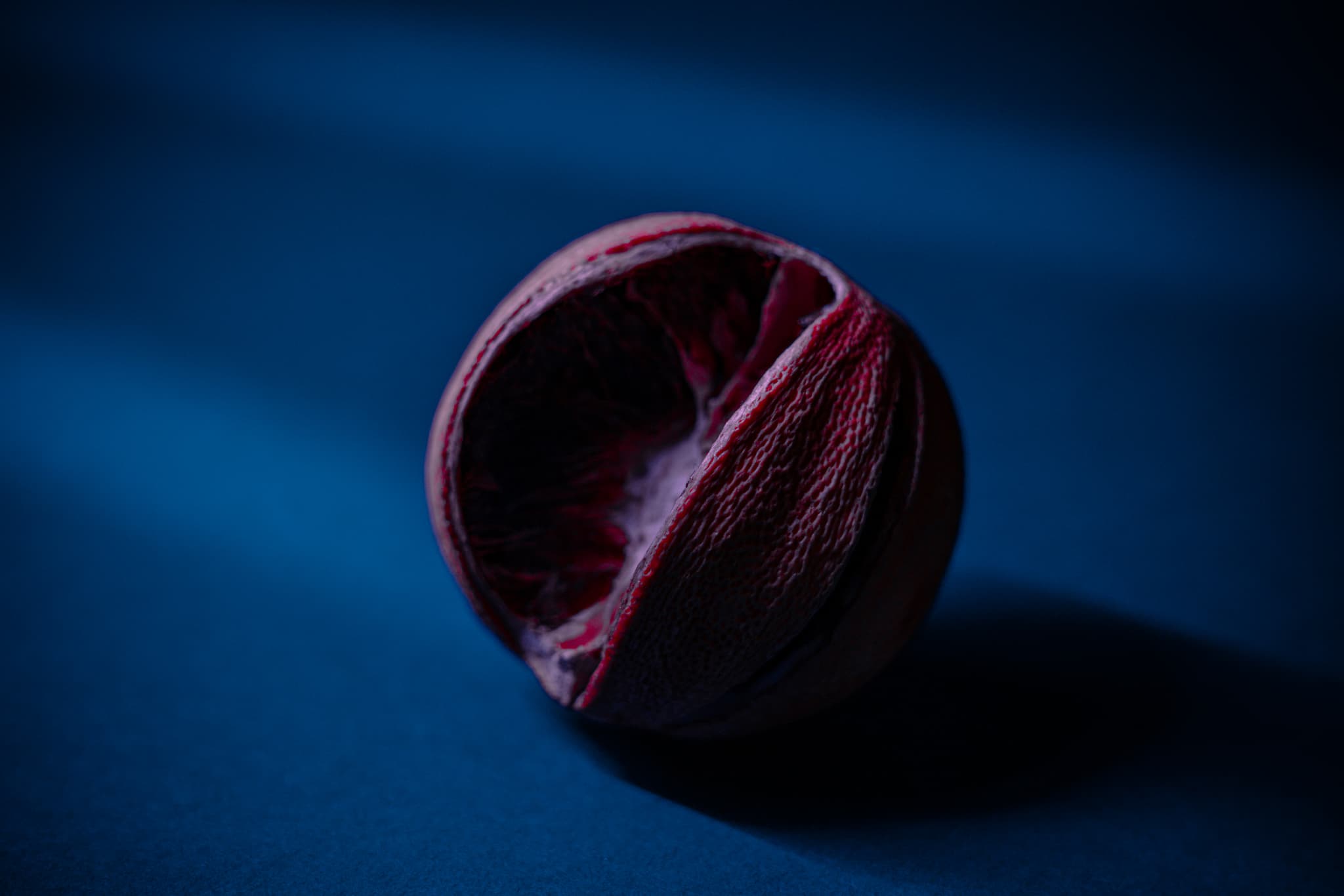 A crimson ball of yarn rests against a dark blue background, highlighted by a subtle light that accentuates its texture and form