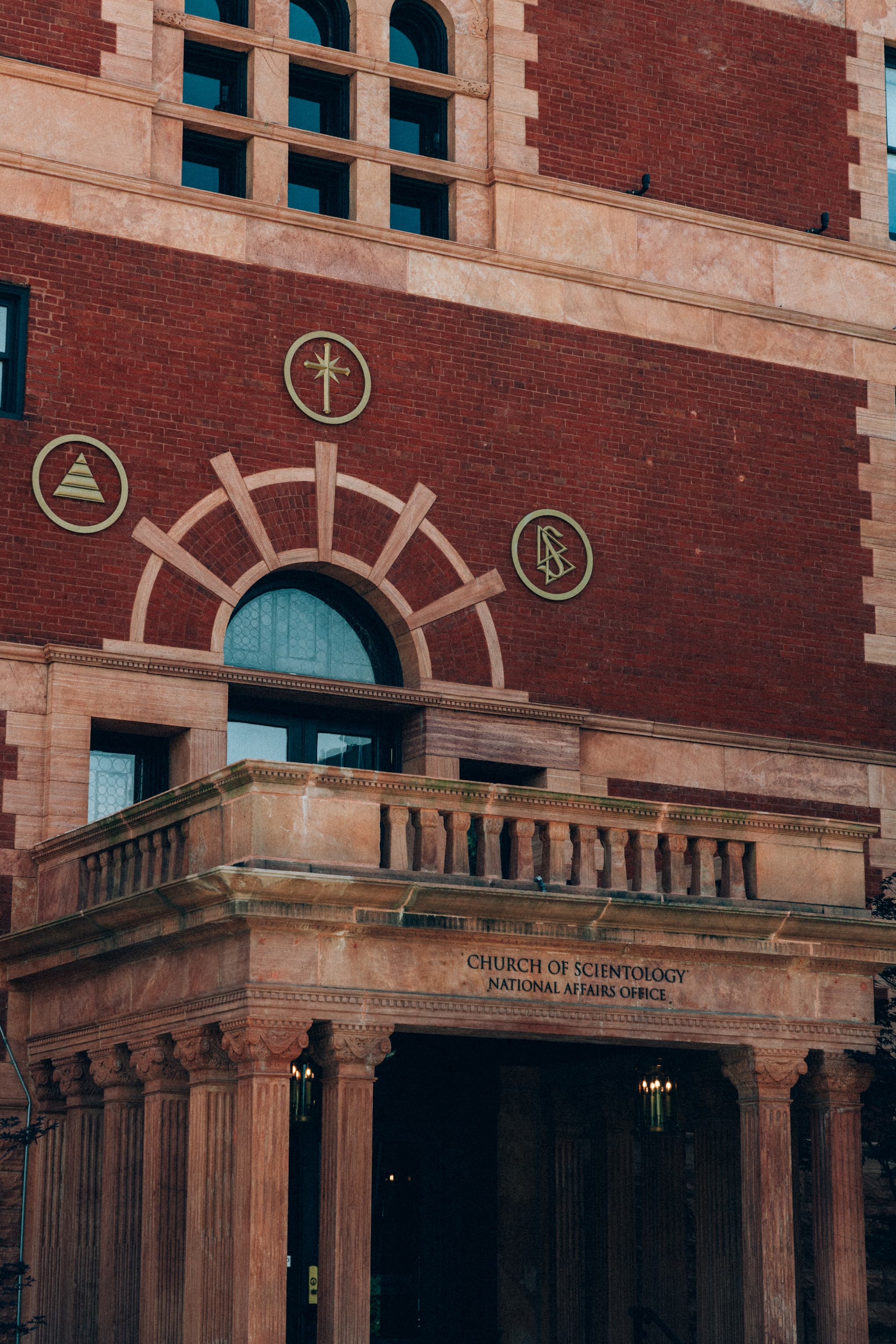 A red brick building with a classical entrance and symbols above the doorway, including a cross within a circle, a triangle, and other circular symbols