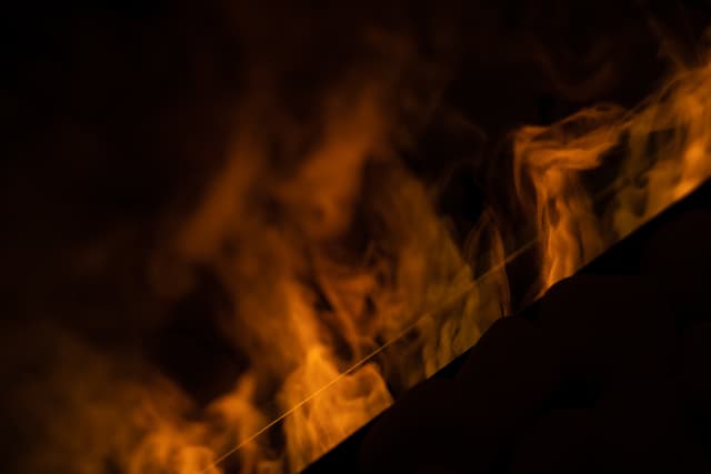 Flames against a dark background, with a hint of a structure's edge visible