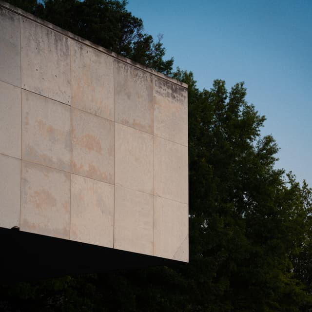 A weathered concrete wall of a building with trees in the background under a clear sky