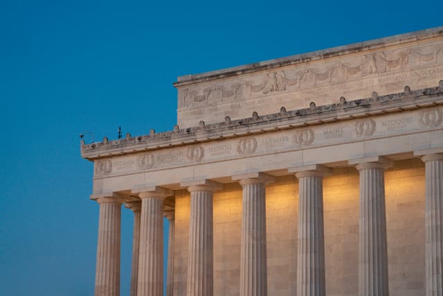 A neoclassical monument with a row of columns lit up against the twilight sky