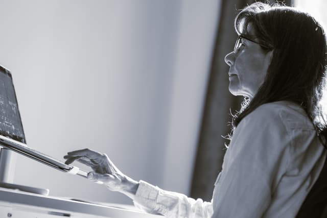 Monica Lopez Vazquez wearing glasses is focused on her work at a computer, with her hand on a mouse The photo is in black and white, capturing a moment of concentration